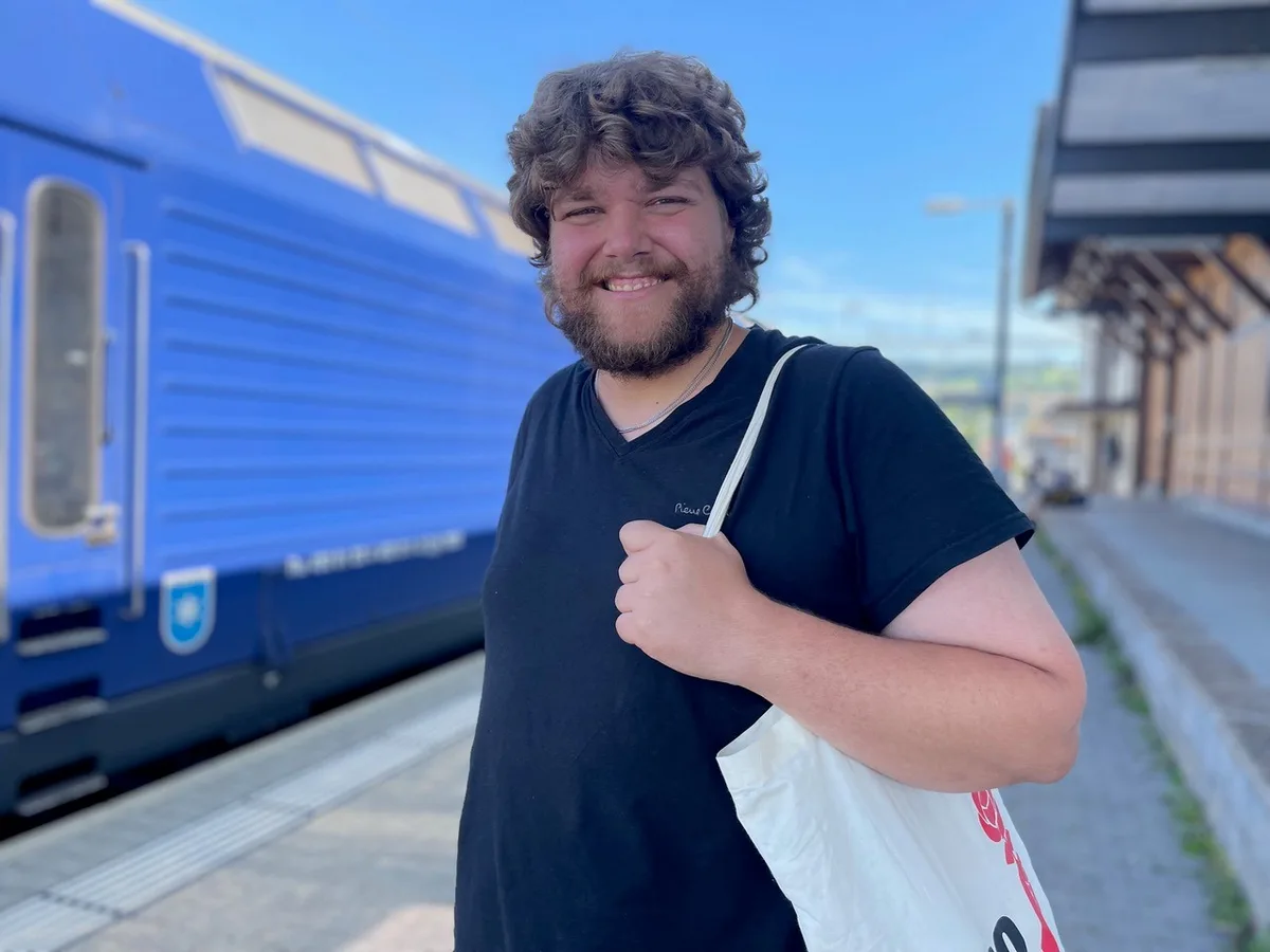 Silas Muggli will in den Gemeinderat von Bubikon. Dabei ist es ihm ein Anliegen, Kommunalpolitik zugänglicher zu machen. Silas Muggli posiert vor einem Zug und lächelt in die Kamera.